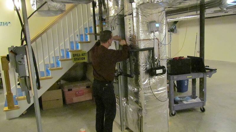 Technician servicing ducted heat pump plant equipment inside a commercial building