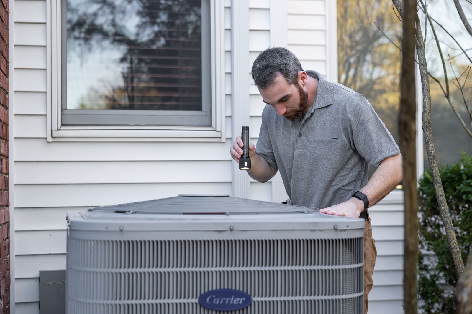 Technician inspecting an outdoor heat pump unit beside a Christchurch home