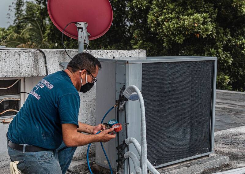 Air conditioning technician checking refrigerant gauges on a rooftop condenser unit